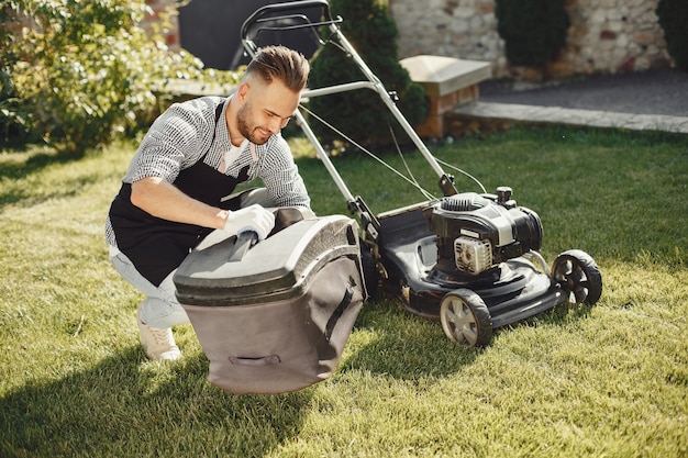Man cutting grass with lawn mover in the back yard. Male in a black apron. Guy repairs.