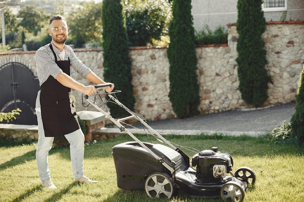 Man cutting grass with lawn mover in the back yard. Male in a black apron.