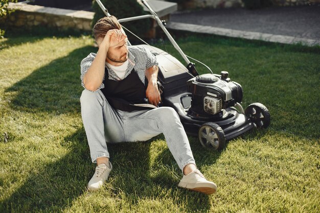 Man cutting grass with lawn mover in the back yard. Male in a black apron.