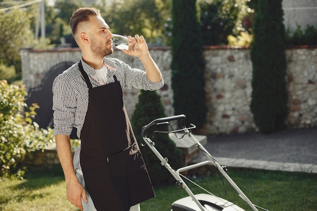 Free photo man cutting grass with lawn mover in the back yard. male in a black apron.