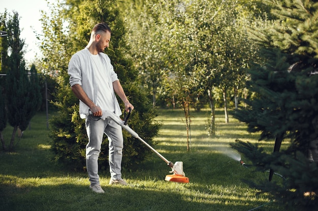 Free photo man cutting grass with lawn mover in the back yard. male in a shirt.