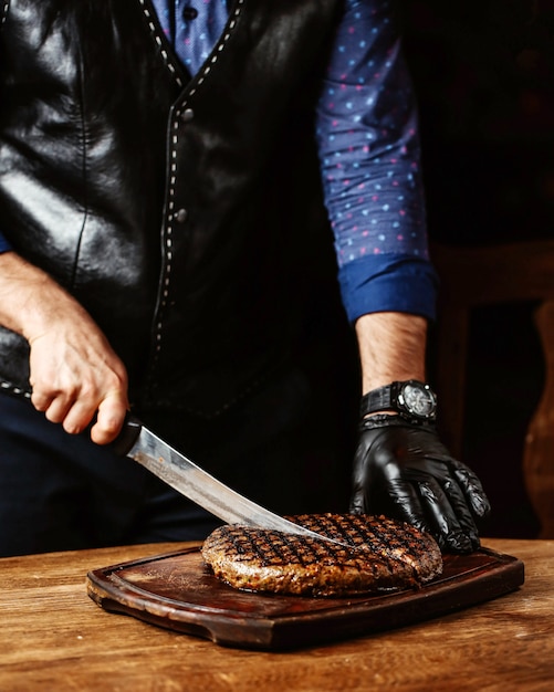 Man cutting steak in round shape wearing black gloves