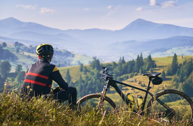 草の上に座って山を見ている男のサイクリスト