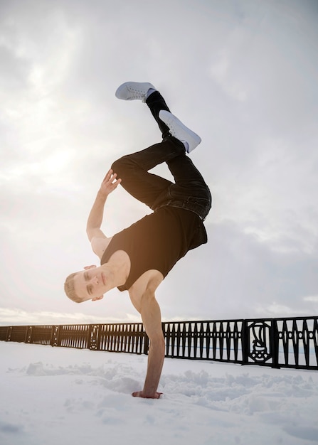 Бесплатное фото Человек танцует под хип-хоп, стоя в одной руке в снегу