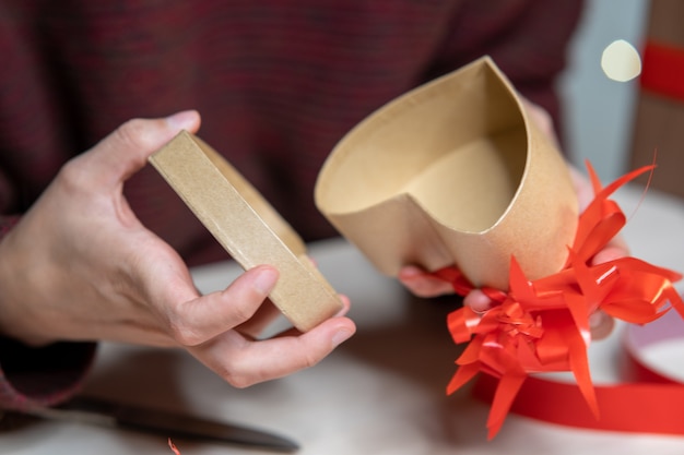 Man decorating a heart-shaped gift box with red ribbons