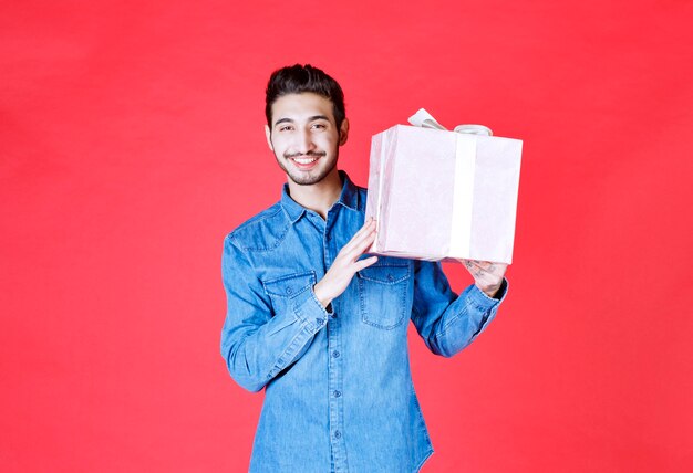 Man in denim shirt holding a purple gift box tied with white ribbon.