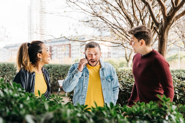 Free photo man in denim talking on phone standing with laughing friends