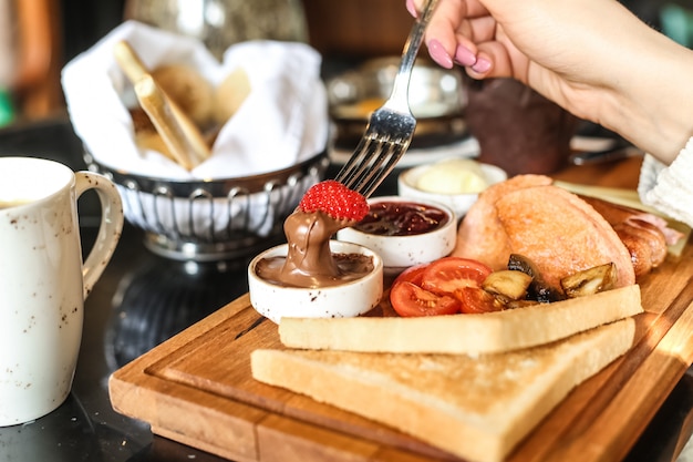 Man dips strawberry in chocolate butter breakfast set toast tomato honey side view