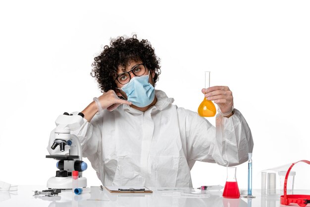 man doctor in protective suit and mask holding flask with yellow solution on white