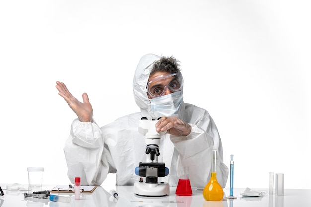 man doctor in protective suit and mask using his microscope on white