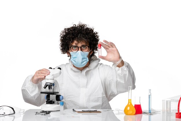 Free photo man doctor in protective suit and mask using microscope holding sample on white