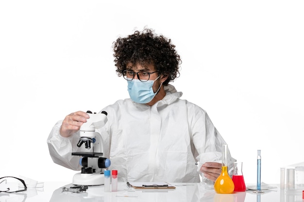 Medico uomo in tuta protettiva e maschera utilizzando il microscopio su bianco chiaro