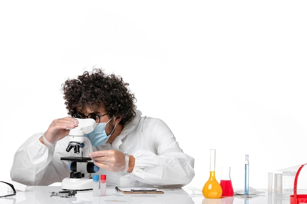 man doctor in protective suit and mask using microscope on a white