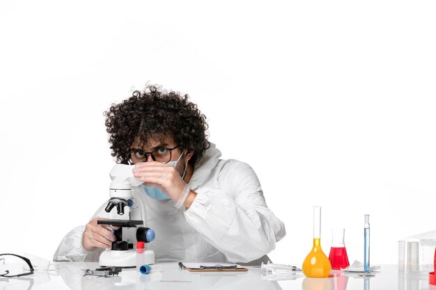 человек-врач в защитном костюме и маске, работающий с микроскопом на белом