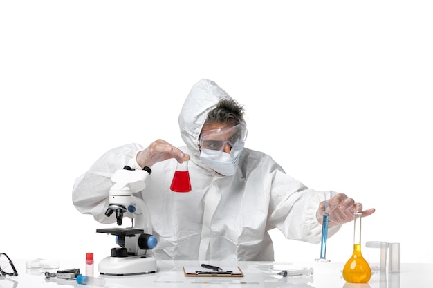 man doctor in protective suit and with mask holding flask with red solution on light white