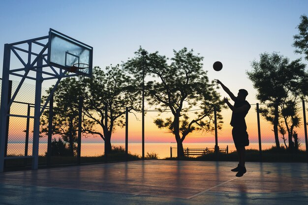 Man doing sports, playing basketball on sunrise, jumping silhouette