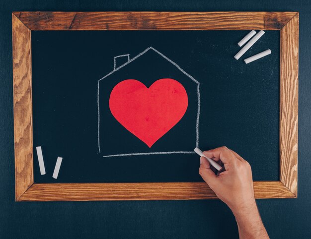 Man drawing house with chalk with heart top view on a frame and black