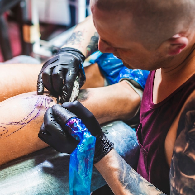Человек рисует татуировку на ноге