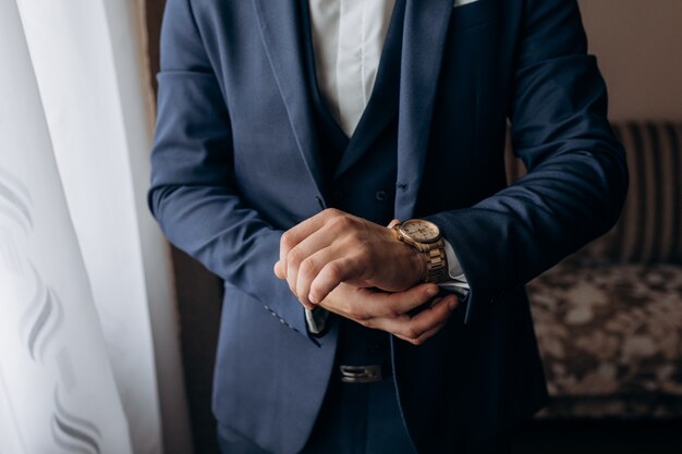 Man dressed in the stylish blue suit, who is putting on elegant watch