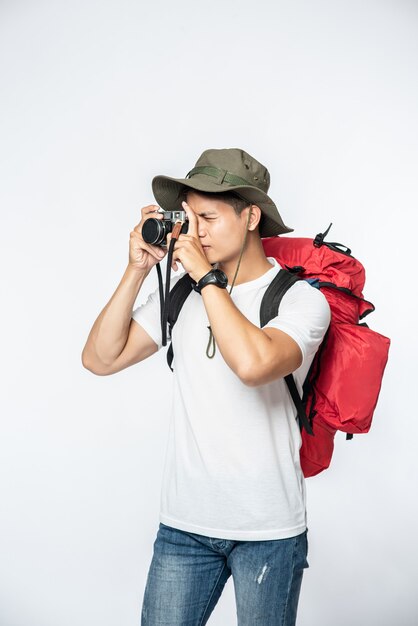 A man dressed to travel wearing a hat and taking a camera