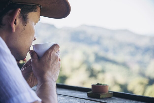 男は緑の丘の背景を持つ熱いお茶を飲む