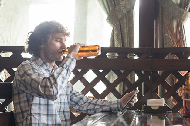 Free photo man drinking beer and using tablet