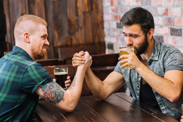 Man drinking beer while arm wrestling with his friend