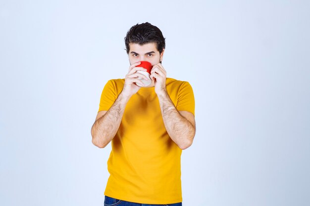 彼の赤いマグカップからコーヒーを飲む男。