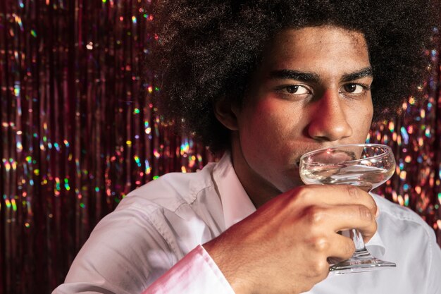 Man drinking a glass of champagne with curtain of sparkles in background