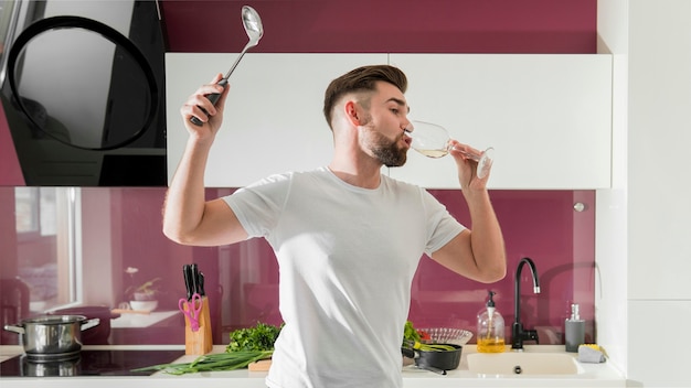 Man drinking wine and fooling around in the kitchen medium shot