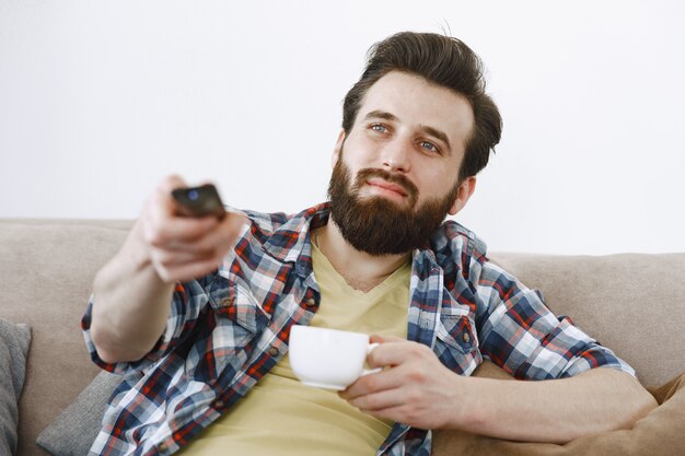 男はコーヒーを飲みます。ソファでテレビを見ている男。手にテレビのリモコン。