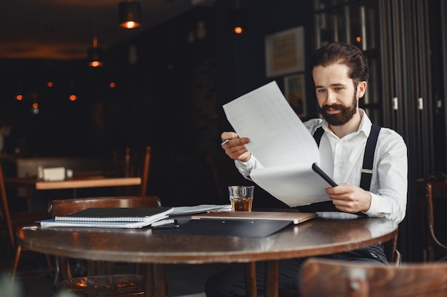 Man drinks whiskey. Businessman reads documents. Director in a shirt and suspenders.