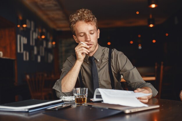 Man drinks whiskey. Businessman reads documents. Director in a shirt and suspenders.