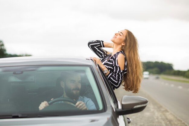 Man driving the car looking at woman leaning out of car window