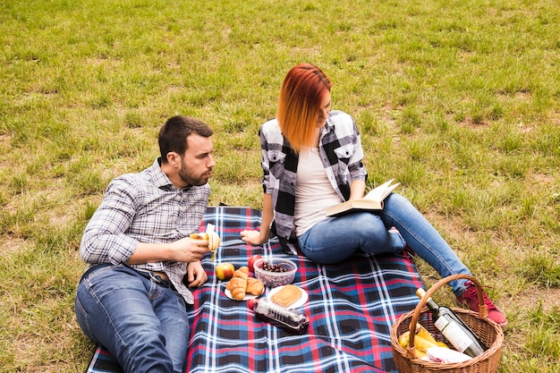 Man eating banana looking at her girlfriend reading book at the picnic