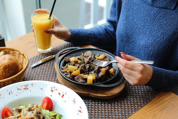 ジャガイモ、玉ねぎ、野菜と揚げた肝臓を食べ、ジュースを飲む男