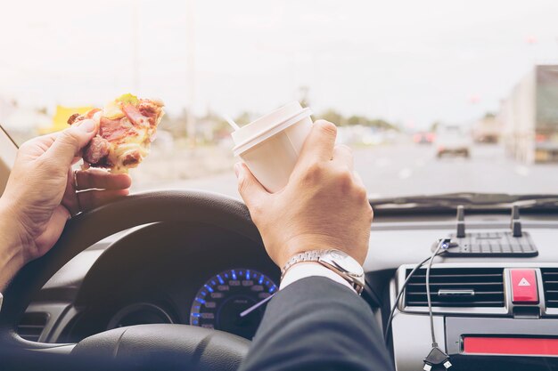 Man eating pizza and coffee while driving car dangerously