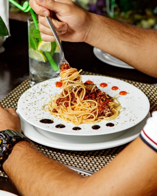 Man eating spaghetti bolognese garnished with dried mint leaves