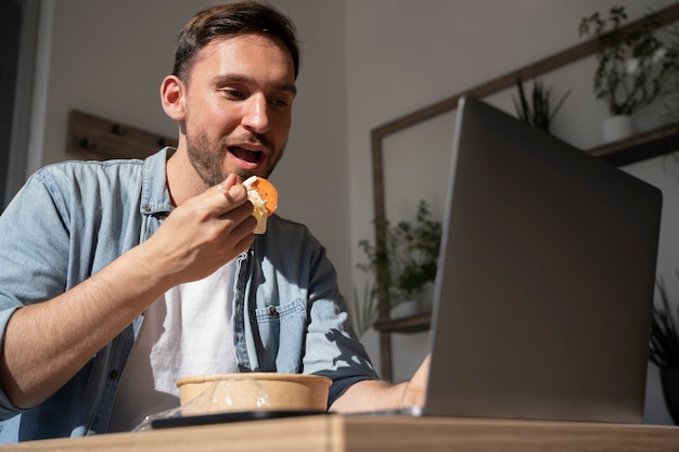 Человек ест еду на вынос и с помощью ноутбука