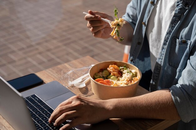 Man eating takeaway food and using laptop