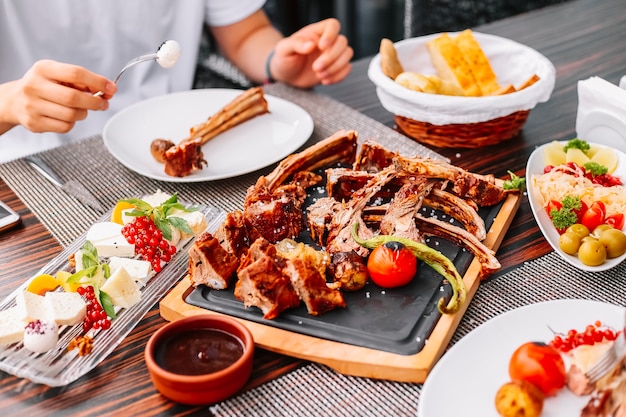 Man eats grilled sliced lamb on the wooden board potato tomato pepper pickles cheese side view