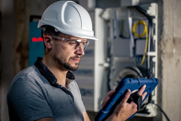 Man an electrical technician working in a switchboard with fuses uses a tablet