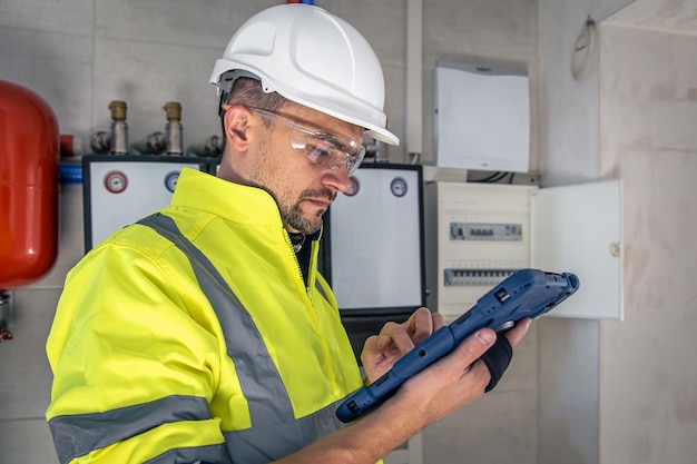 Foto gratuita l'uomo un tecnico elettrico che lavora in un quadro elettrico con fusibili utilizza un tablet