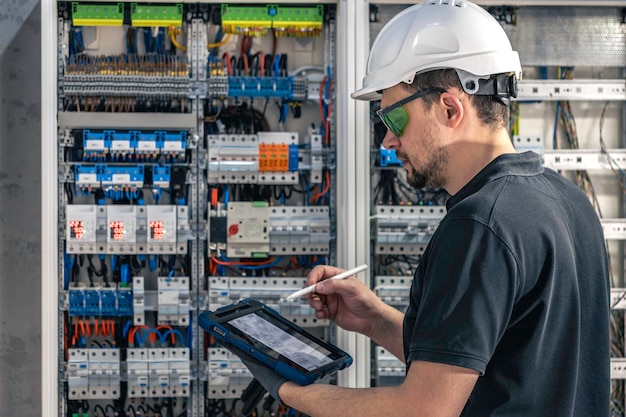 Free photo man an electrical working in a switchboard with fuses uses a tablet