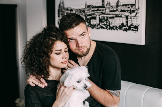 Man embraces tender curly woman with little dog in her arms