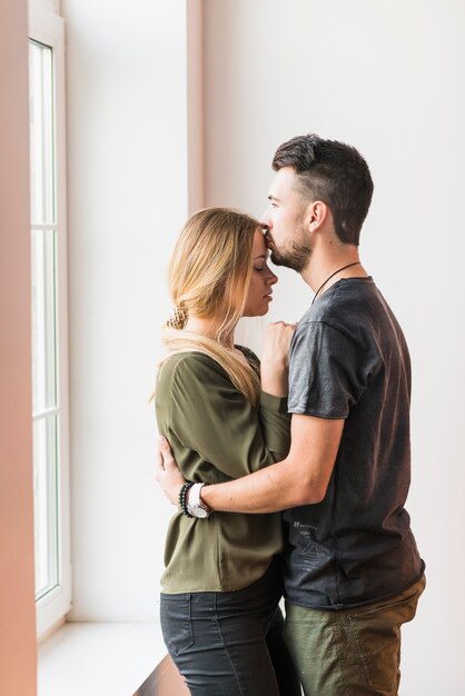 Man embracing her girlfriend kissing on her forehead at home