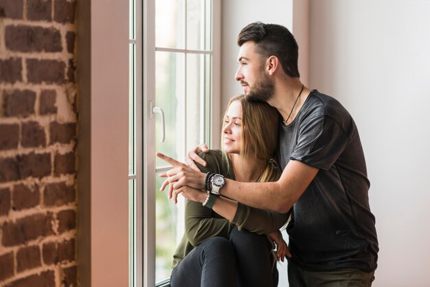 Man embracing her girlfriend pointing at something near the window