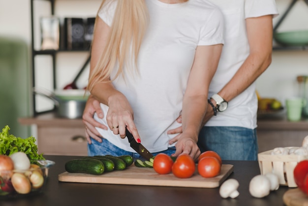 Man embracing her wife while cutting vegetables on kitchen counter