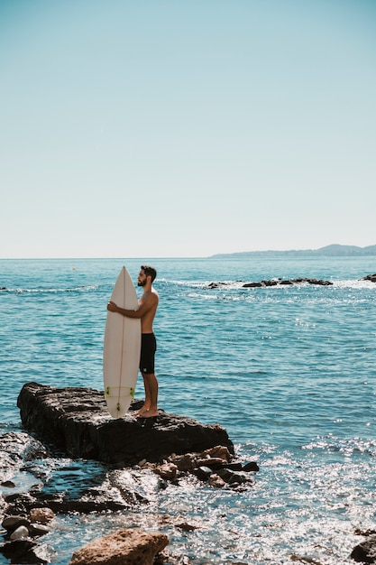 Free photo man embracing surfboard on stone