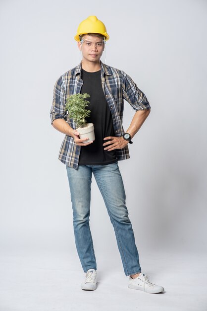 A man in an engineering hat and stood holding a plant pot in his house.